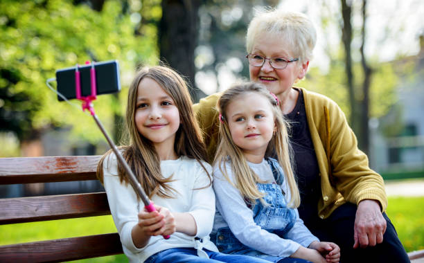 bonne famille. grand-mère s’asseyant dans le stationnement avec des petites-filles et prenant un selfie avec le smartphone. concept de style de vie - making memories photos et images de collection