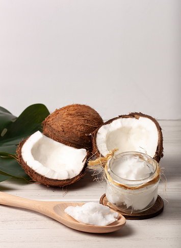 Still life of two coconuts, one of them cut in half, with a jar of coconut oil on a  white background