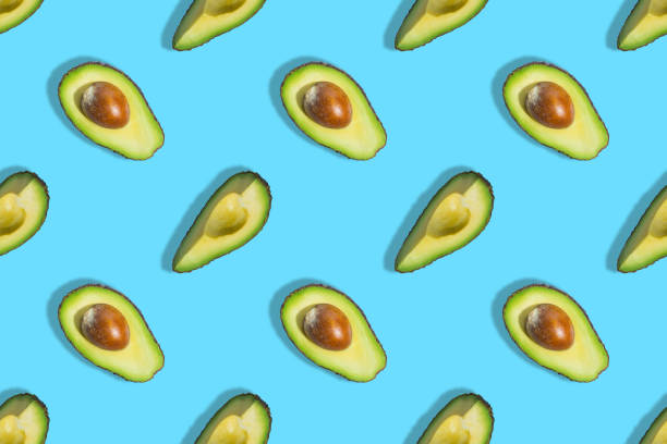 istock Seamless pattern of fresh ripe green avocado fruit half isolated on blue background. Top view. Banner. Flat lay composition. Pop art design. Creative summer food background 1306725614