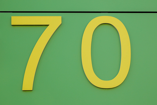 Yellow number seventy on a green house wall, background for a birthday template, no person