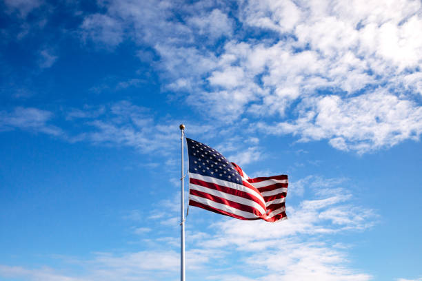 istock American Flag Blowing Against Vibrant Blue Sky 1306728158