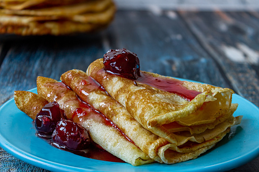 Fresh pancakes with cherry jam on a blue plate.