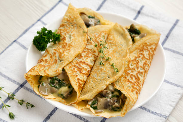 istock Savory Homemade Mushroom, Spinach and Cheese Crepes on a white plate on cloth, low angle view. Close-up. 1306731193