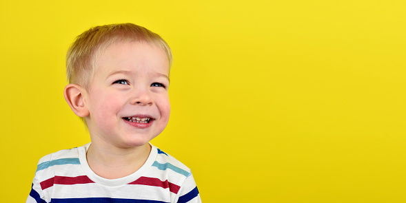 Happy smiling little boy on color background. Portrait of a beautiful European boy two years old on a yellow background. Copy space for text.