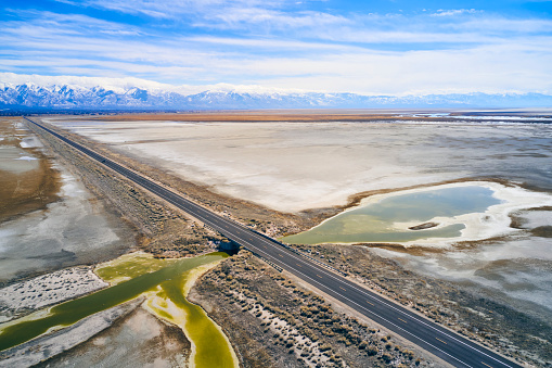 An aerial view of an empty straight road on a causeway under blue sky in a Utah winter.