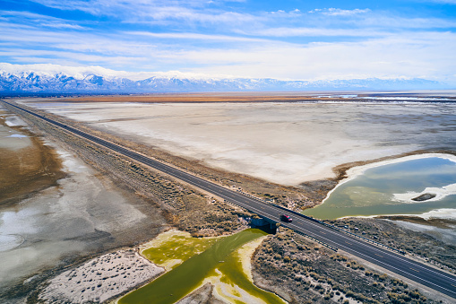 An aerial view of an empty straight road on a causeway under blue sky in a Utah winter.