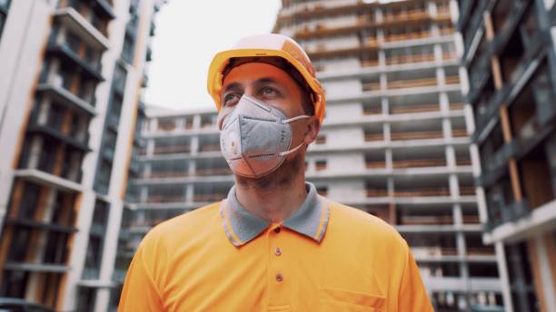 istock Construction worker wearing safety equipment. KN 95 mask. Corona mask. Covid-19 protective respirator. Coronavirus outbreak. Builder works in protective equipment respirator and hard hat 1306747716