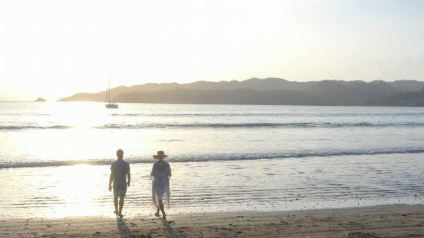 istock Mature couple walks down sandy beach at sunrise 1306757725