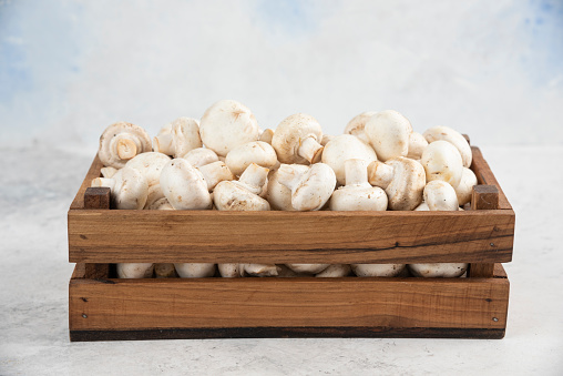 White mushrooms inside a wooden tray on a marble background. High quality photo