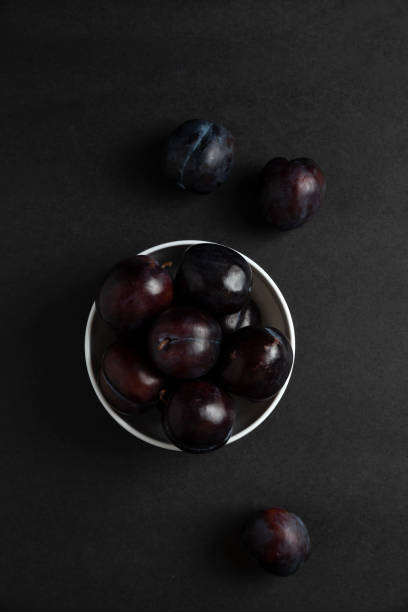 istock Black plums in white ceramic saucer, top view 1306762459