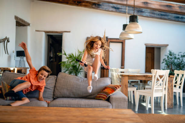 istock Young Boy and Girl Jumping Over Sofa with Remote Control 1306762547