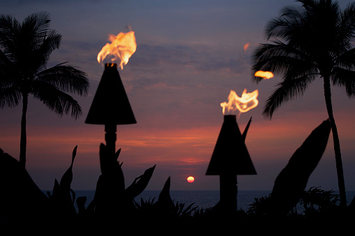 Close-up of tiki torches and palm trees framing a beautiful Hawaiian sunset over the Pacific Ocean