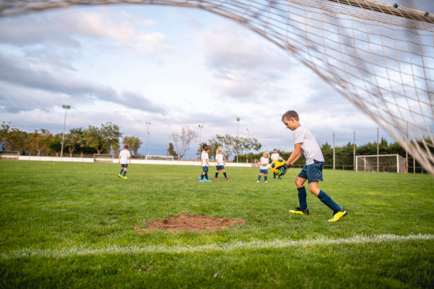 Pre-Teen Boy Goalie Preparing to Kick Ball Down Field Personal perspective beneath netting of young boy goalie preparing to kick ball down field during practice session. 6 9 months stock pictures, royalty-free photos & images