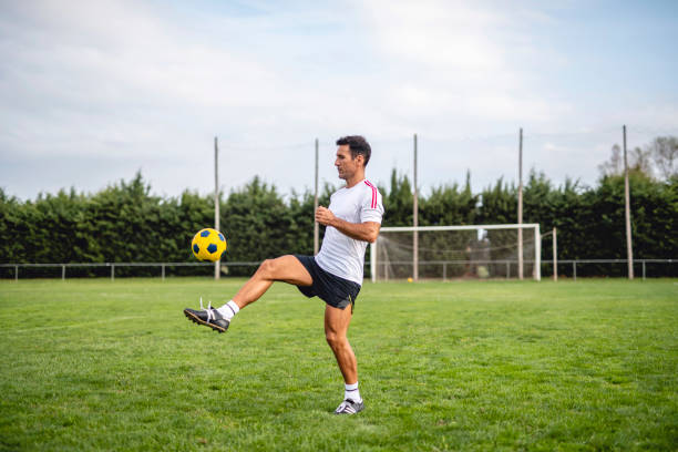 Mature Male Footballer Practicing Juggling for Ball Control Action portrait of fit Caucasian male footballer in early 40s practicing juggling to maintain ball control skills. soccer soccer ball kicking adult stock pictures, royalty-free photos & images
