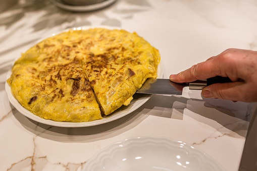 Hands of an elderly woman cutting a portion of a Spanish omelet.
