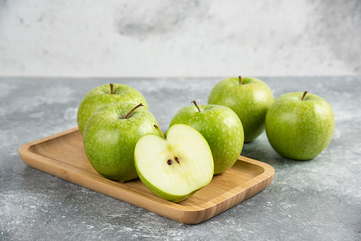 Bunch of whole and sliced green apples on wooden plate. High quality photo