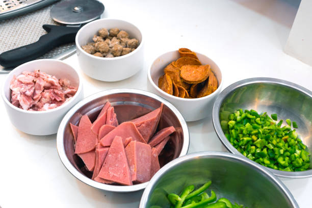 istock Pizza ingredients arranged in white bowls - Beef, ham, bacon, pepperoni, chopped bell peppers. A Pizza slicer is nearby. Preparation concept. 1306782417