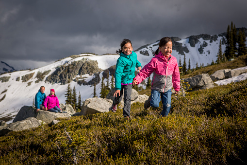 Girls running and playing in mountains while parents are watching them, sitting in background.