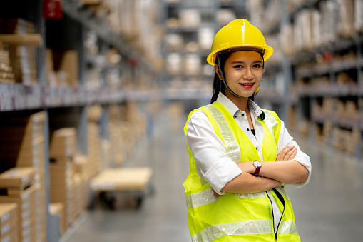 Young smiling woman worker and vest checking box in stock in  factory warehouse, Staff check stock girl prepares shipping goods and packaging products to customer.