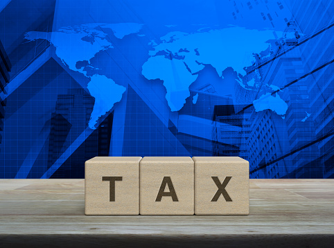 TAX letter on block cubes on wooden table over world map, modern office city tower and skyscraper, Business and finance concept, Elements of this image furnished by NASA