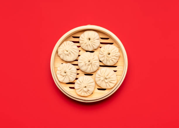 Raw baozi dumplings in a bamboo steamer, top view.  Cooking Chinese steamed dumplings Uncooked pork baozi dumplings in bamboo steamer, isolated on red colored background. Raw Chinese food, flat lay. Cooking steamed bao buns, above view. chinese dumpling stock pictures, royalty-free photos & images