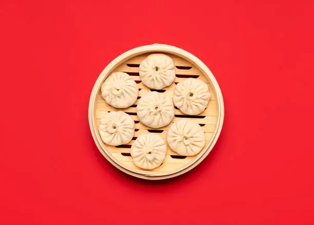 Uncooked pork baozi dumplings in bamboo steamer, isolated on red colored background. Raw Chinese food, flat lay. Cooking steamed bao buns, above view.