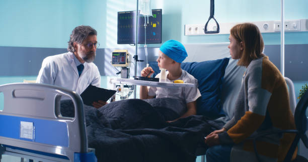 Doctor speaking with mother and eating little patient Bearded mature oncologist with clipboard talking with adult woman and eating boy in ward of modern hospital real time stock pictures, royalty-free photos & images