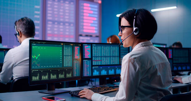 Young woman trading stocks in office Back view of young female trader with headset speaking and browsing data on computer while working in office of stock exchange company real time stock pictures, royalty-free photos & images
