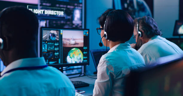 Multiracial operators working in flight control center Back view of diverse men and women in headsets using computers and speaking while working in mission control center together real time stock pictures, royalty-free photos & images