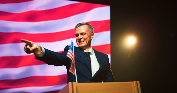 African American mature politician standing at platform and presenting is report at formal conference