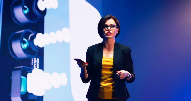istock Female speaker with new smartphone talking against LED screen 1306804822