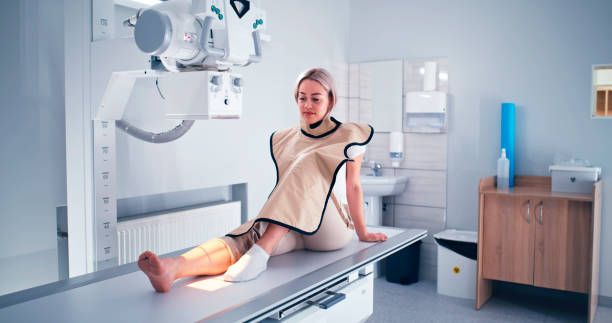 Friendly doctor preparing patient for X ray scanning Protective apron on smiling young woman while working in X ray lab in clinic real time stock pictures, royalty-free photos & images