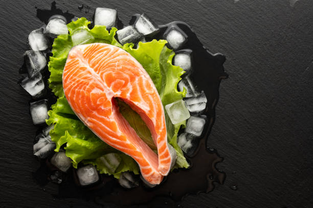 istock chilled salmon steak in lettuce and ice on a stone background, top view, place for text 1306805214