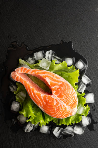 istock chilled salmon steak in lettuce and ice on a stone background, top view, place for text 1306805391