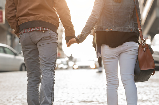 Couple holding hands and walking on a sidewalk.