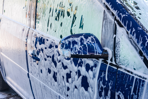Car wash, a person at a self-service car wash, under a stream of pressure puts foam on the car.2020