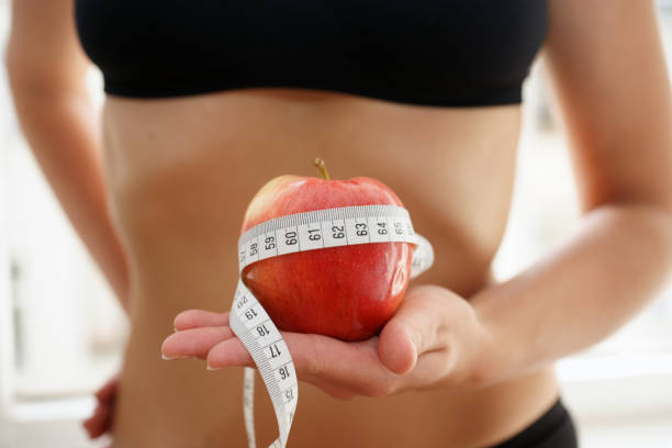スポーツ衣装の若いスリムな女性は、メジャーテープ栄養ダイエットでリンゴを保持しています - abdomen women waist slim ストックフォトと画像