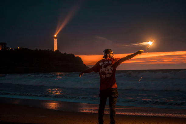 un jeune homme avec un sparkler sur un coucher de soleil à la plage de la petite maison de l’amour dans biarrtiz. france - northumberland england bamburgh lighthouse beach photos et images de collection