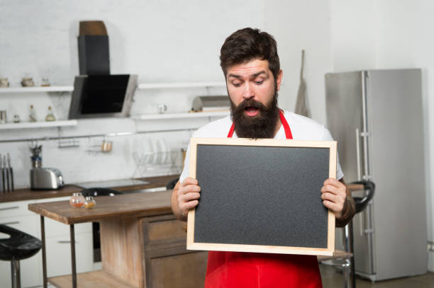 istock Secret tips. Useful information. Man bearded hipster red apron stand in kitchen. Kitchen furniture store. Kitchen hacks concept. Clever ways to organize kitchen. Cook hold blank chalkboard copy space 1306815210