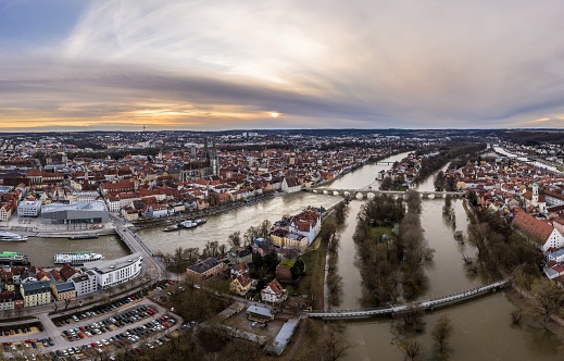 Panorama of Regensburg city in Bavaria with the river Danube the cathedral and the stone bridge during flood and snowmelt at sunset, Germany