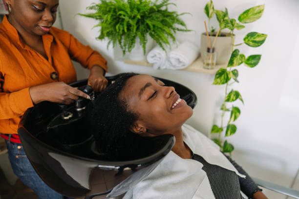 Washing hair in a hair salon Photo of an African American hairdresser, washing hair to a customer with an Afro hair style black woman washing hair stock pictures, royalty-free photos & images