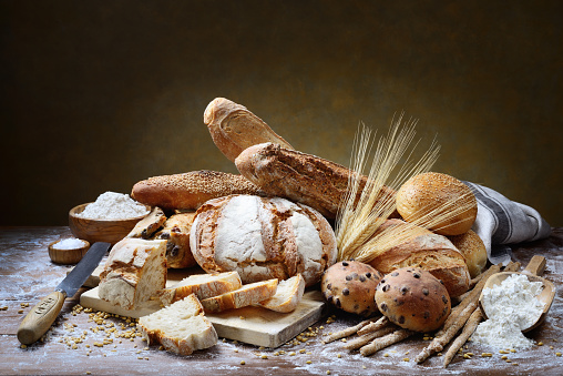 Loaves, baguettes, buns and other artisanal breads in rustic setting.