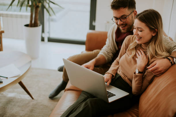 istock Young couple using laptop together while sitting on sofa at home 1306826053