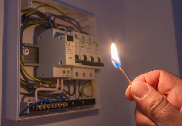 Blackout or power outage,  concept image. Person's hand in complete darkness holding a burning matchstick to investigate a home electricity fuse box.