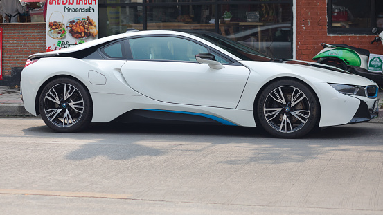 Sideview of white colored BMW i8 sports car parked in street of Bangkok Ladprao. In background are restaurants