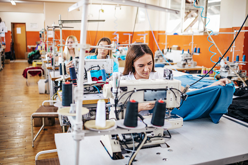 Professional seamstresses work in tailoring or sewing industry production hall.