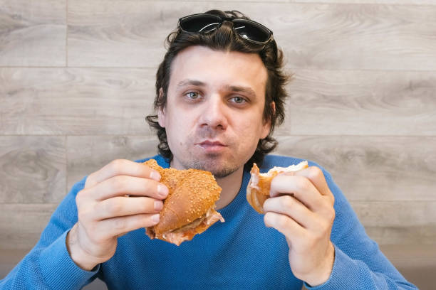 istock Man eating a hotdog and shawarma simultaneously sitting in cafe. 1306844280