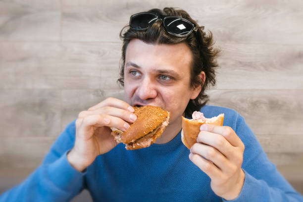 istock Man eating a hotdog and shawarma simultaneously sitting in cafe. 1306844282