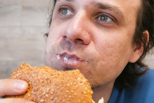 Portrait of young man eating a hamburger sitting in a cafe
