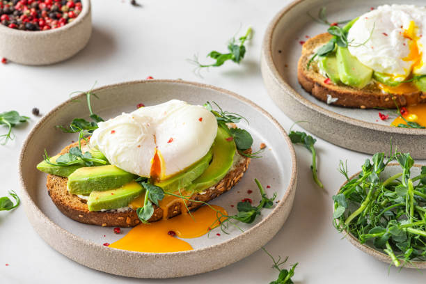 istock Healthy breakfast. Whole wheat toasted bread with avocado, poached egg, soft cheese and sprouts on white background 1306846594